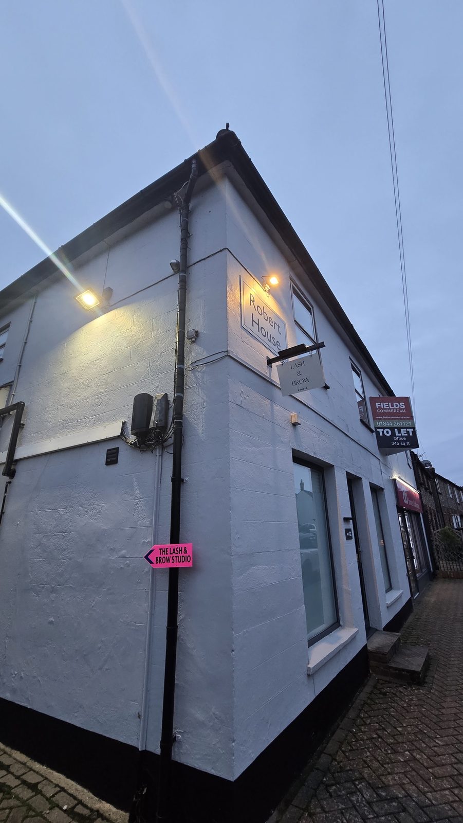 The white corner building on Station Road at dusk, with the studio sign lit